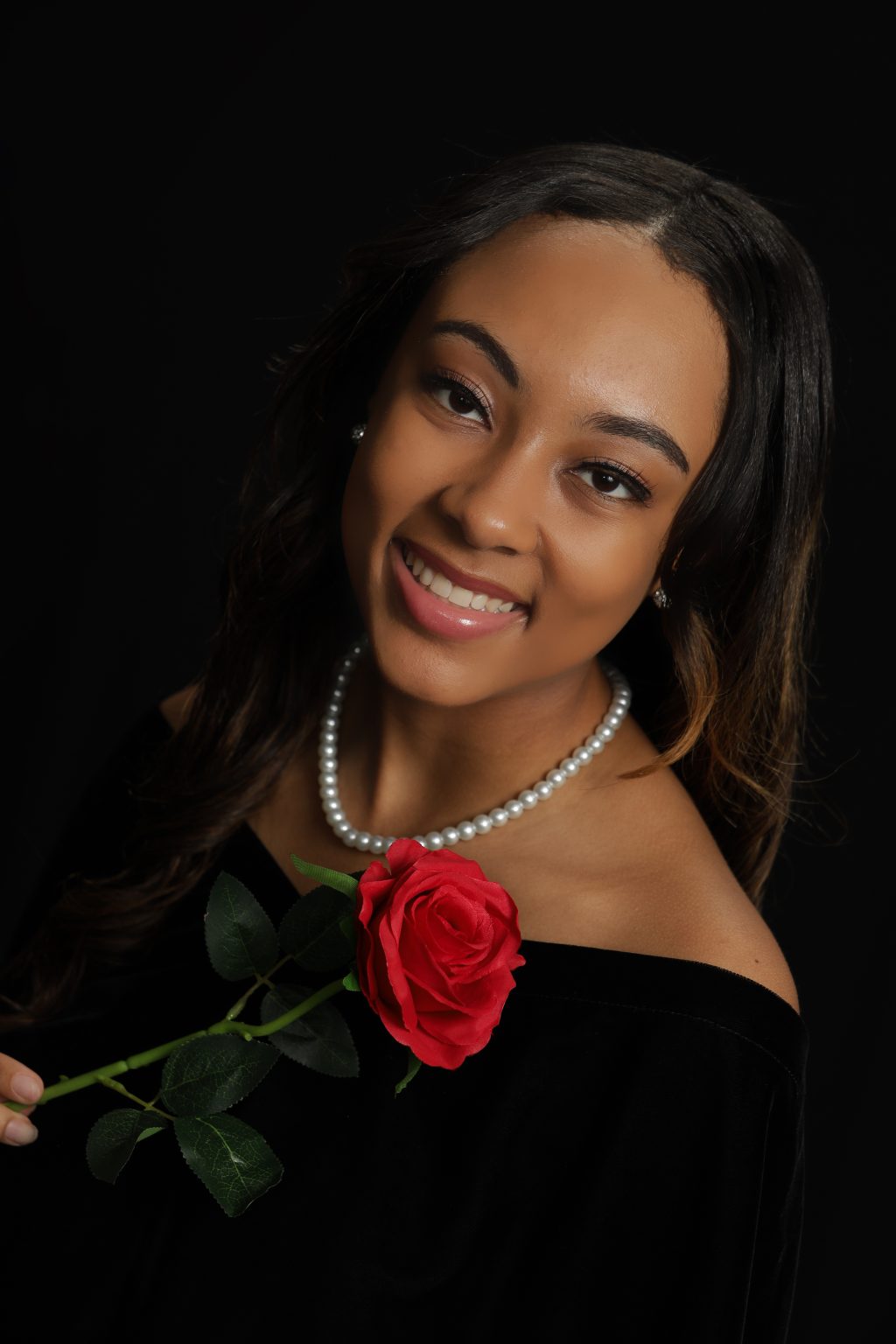 An image of a senior girl posing with a rose in traditional senior photo clothing.